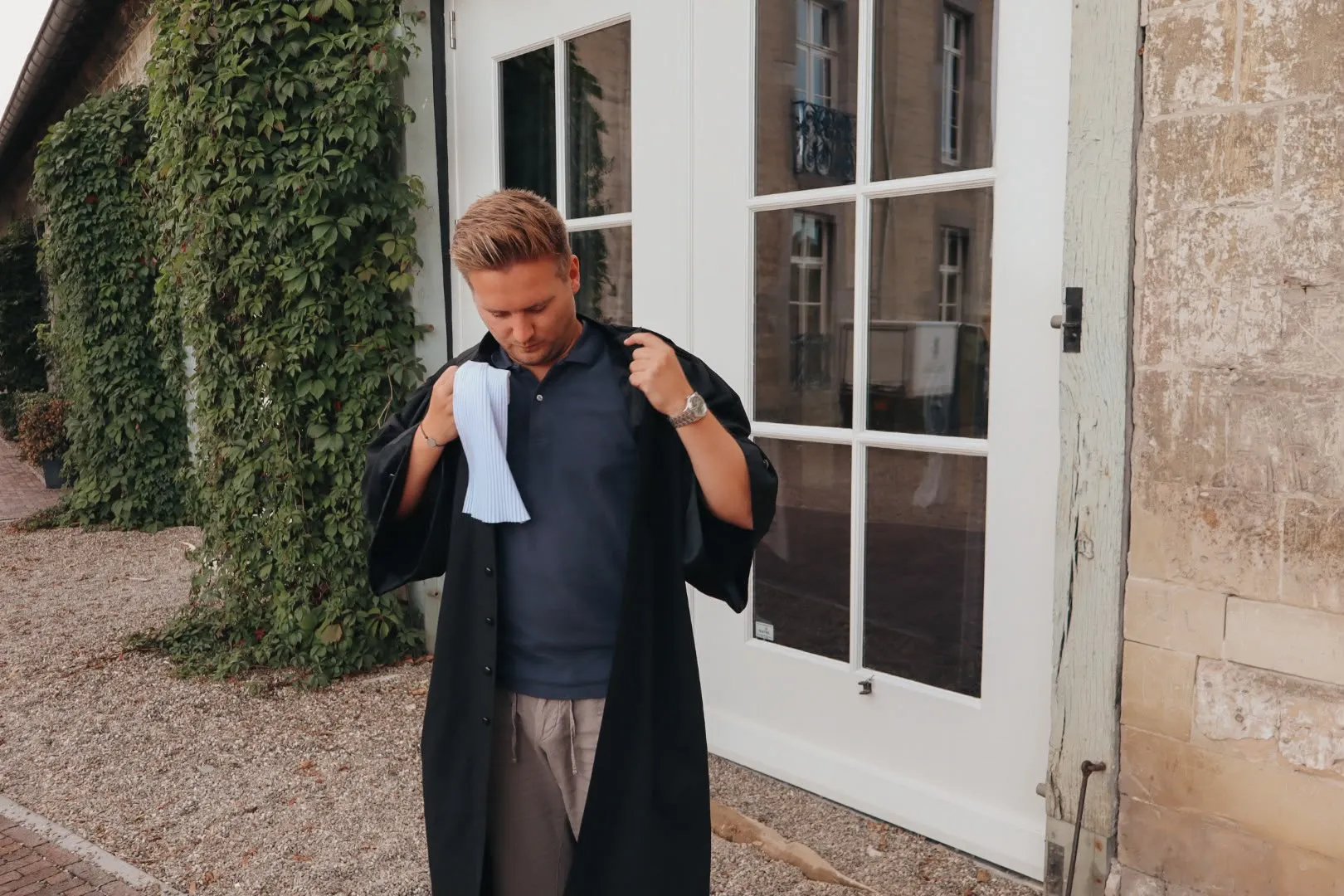Sander Eycken trekt zijn toga aan bij een met klimop begroeide gevel